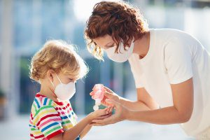 Masked mother putting hand sanitizer on masked child's hands